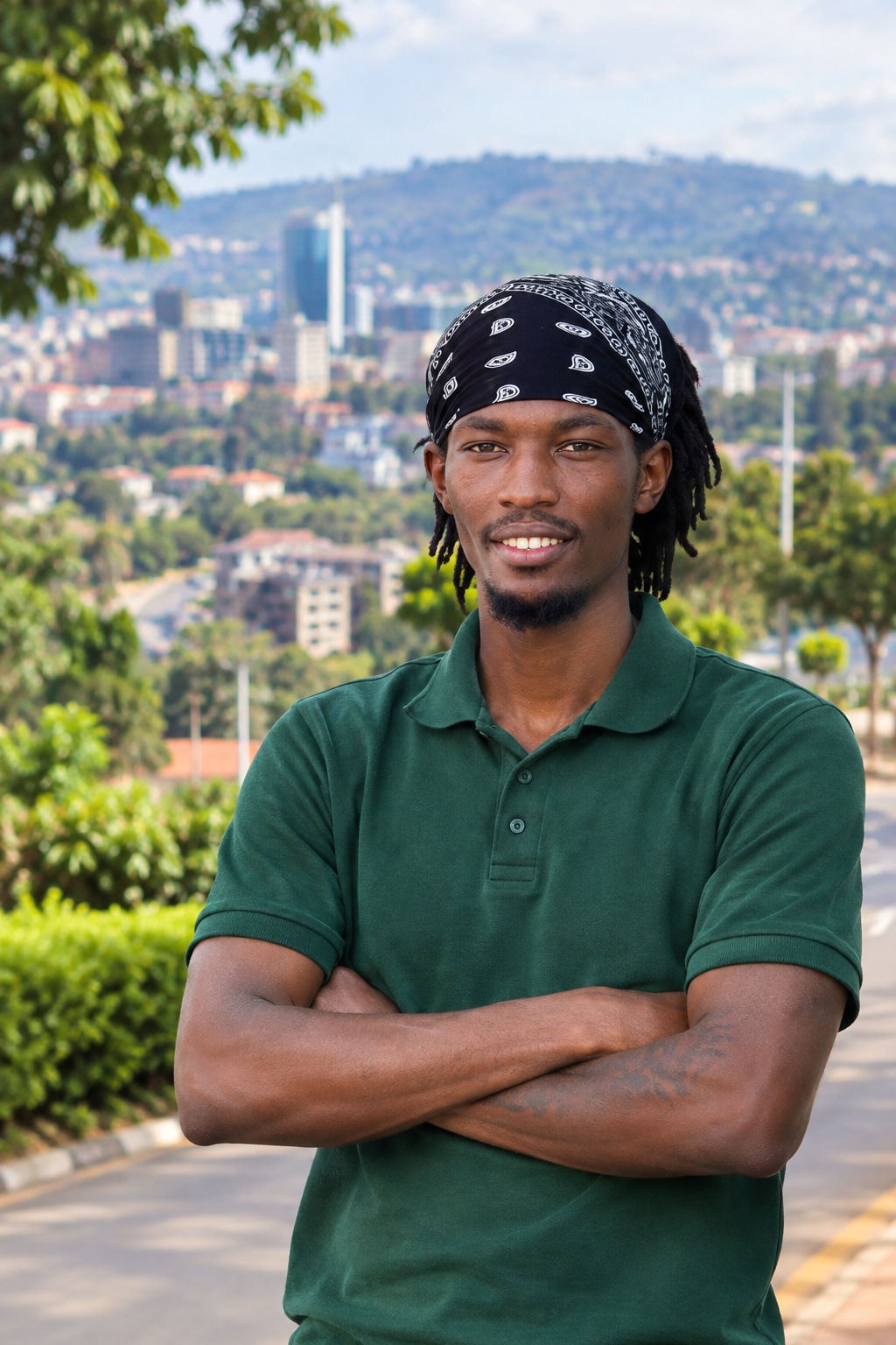 Discover Kigali on Foot guide smiling in a green polo shirt with arms crossed against a softly blurred Kigali hillside skyline